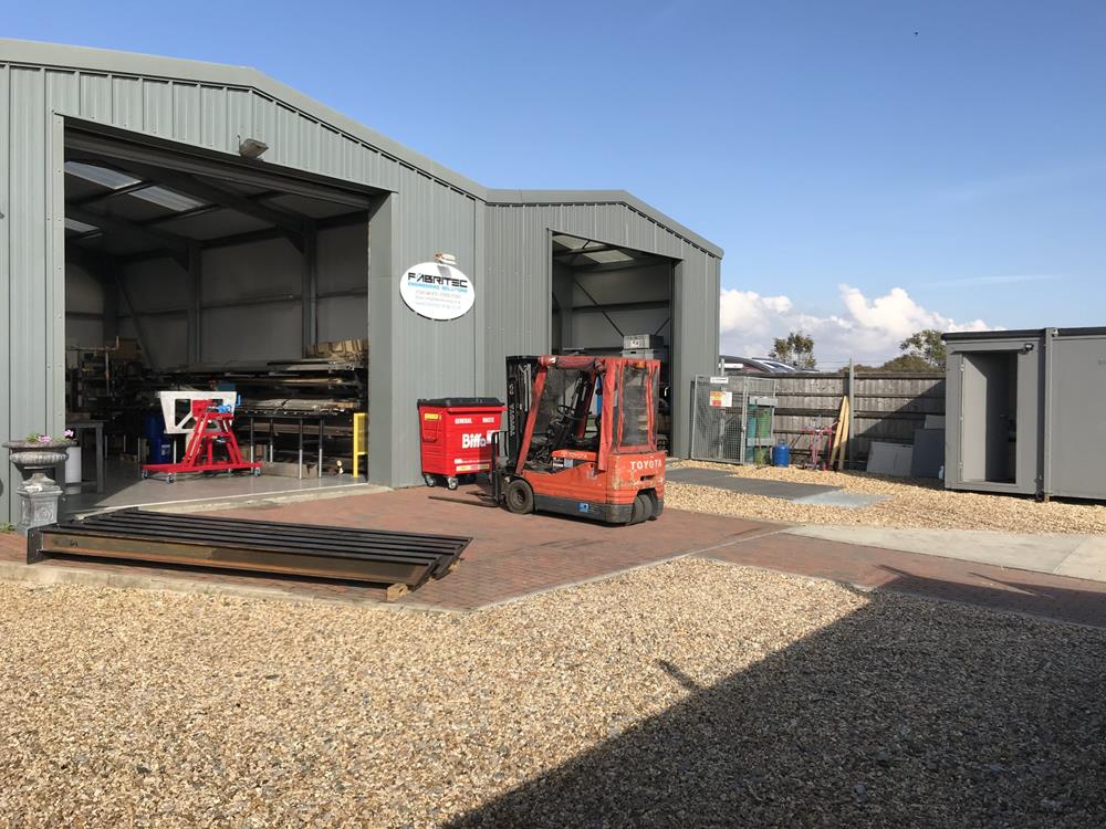 An external view of the Fabritec unit in Sidlesham near Chichester. Shown with the main roller shutter doors open and a forklift truck outside.