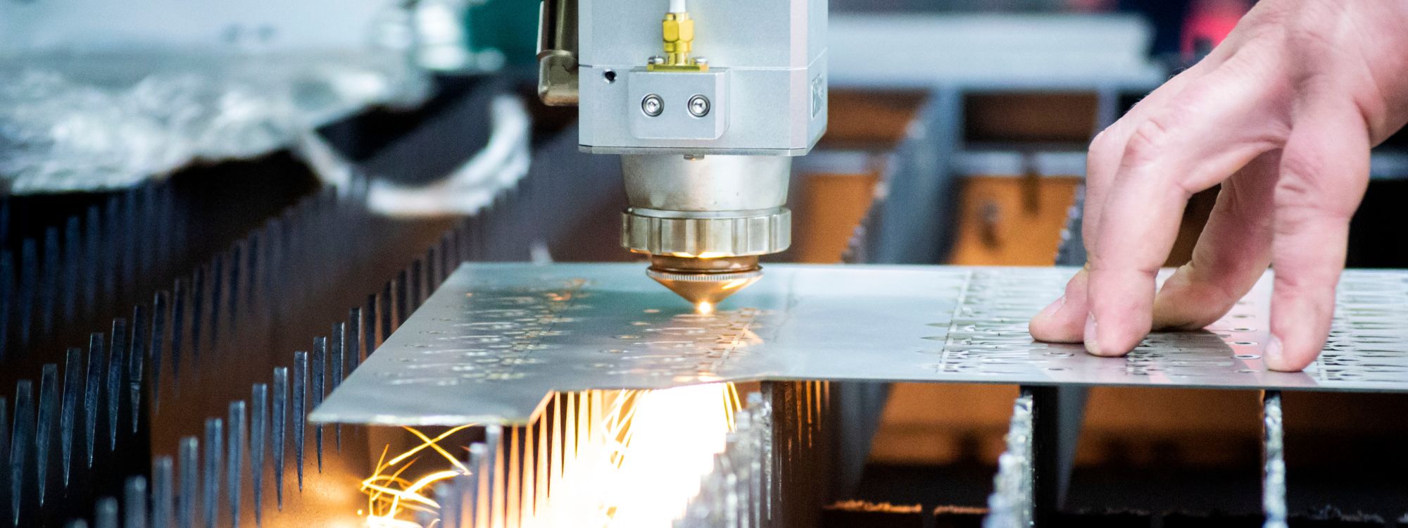 A close up of a laser cutting machine with an operator's hand guiding the steel into the cutting beams.