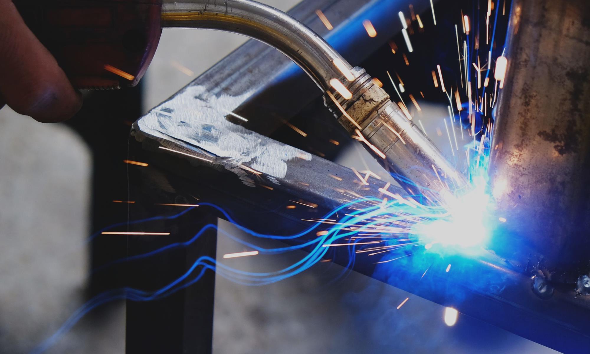 A welder doing welding with sparks flying from the end of the torch.